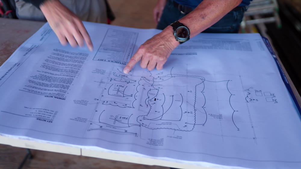 Hands spread across a set of plans on a folding table at a framing site